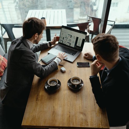 Two young businessman having a successful meeting at restaurant. Two businessmen talking about new opportunities sitting with laptop at desk, planning project, considering business offer, sharing ideas while drinking coffee together